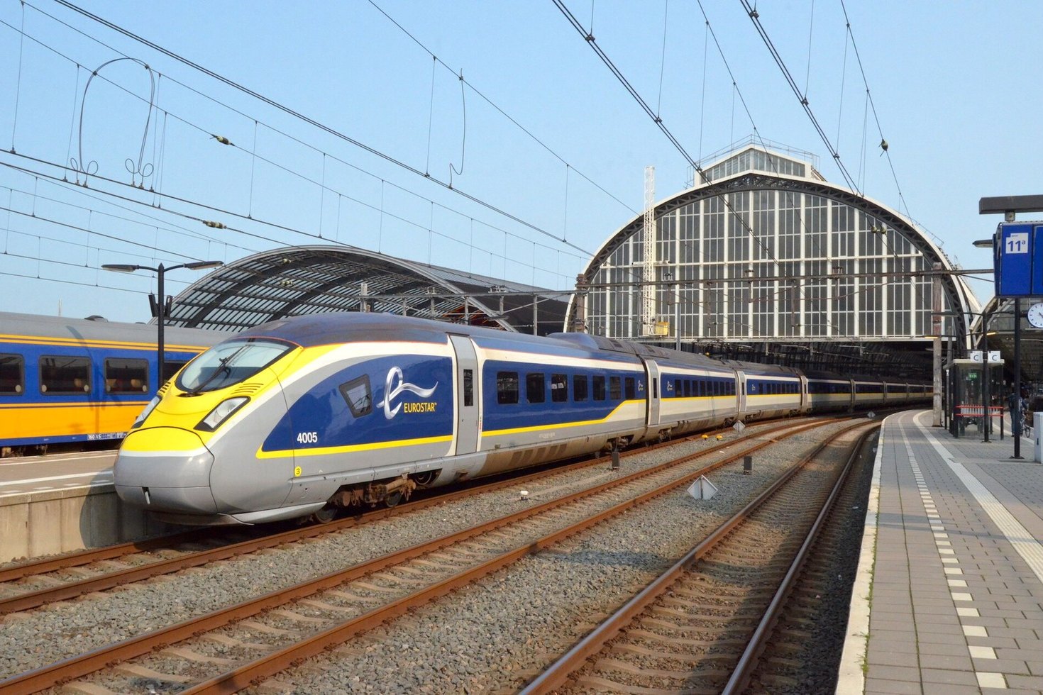 A blue and yellow Eurostar train, unit 4005, standing at Amsterdam Centraal under the station's arched iron and glass train shed on a clear day