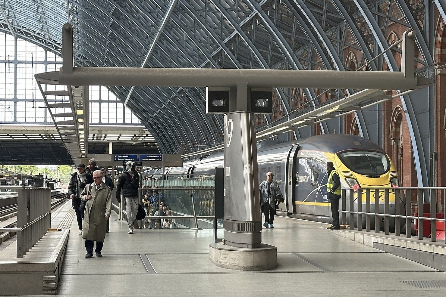 A blue and yellow Eurostar train at a platform under the iron roof of St Pancras station in London, with passengers walking along the platform