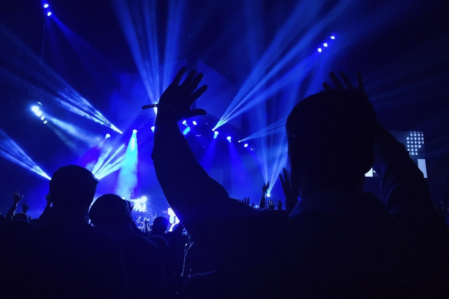 A crowd with arms in the air in front of a stage lit by blue beams