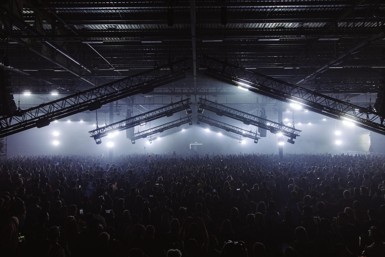 The vast interior of Drumsheds in Tottenham, thousands of people under angled lighting trusses, the largest of the four London rooms compared