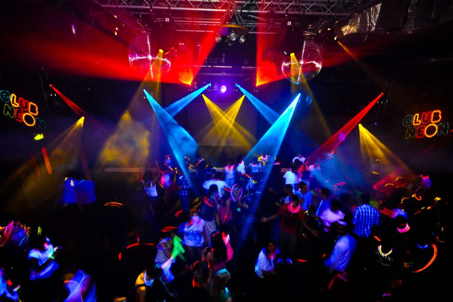 A neon-lit club dancefloor packed with students, seen from above