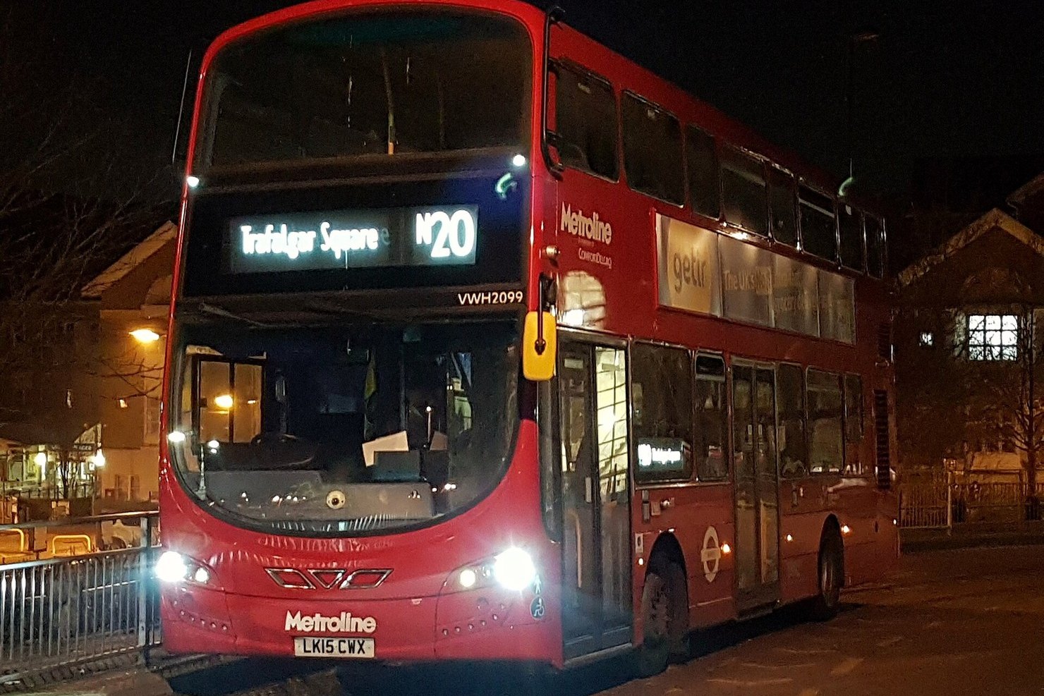 A red London double-decker night bus with N20 Trafalgar Square on its destination blind, headlights on, at night