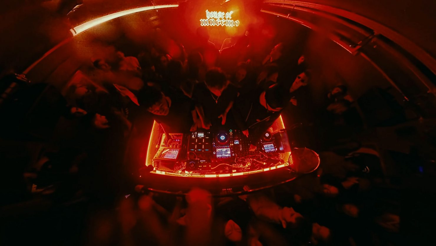 MNEEMO (Yaroslav Gorovoy) performing at a club with a glowing red-lit console. Crowd surrounds, enjoying the music. "house of vansnemo" text is visible above.
