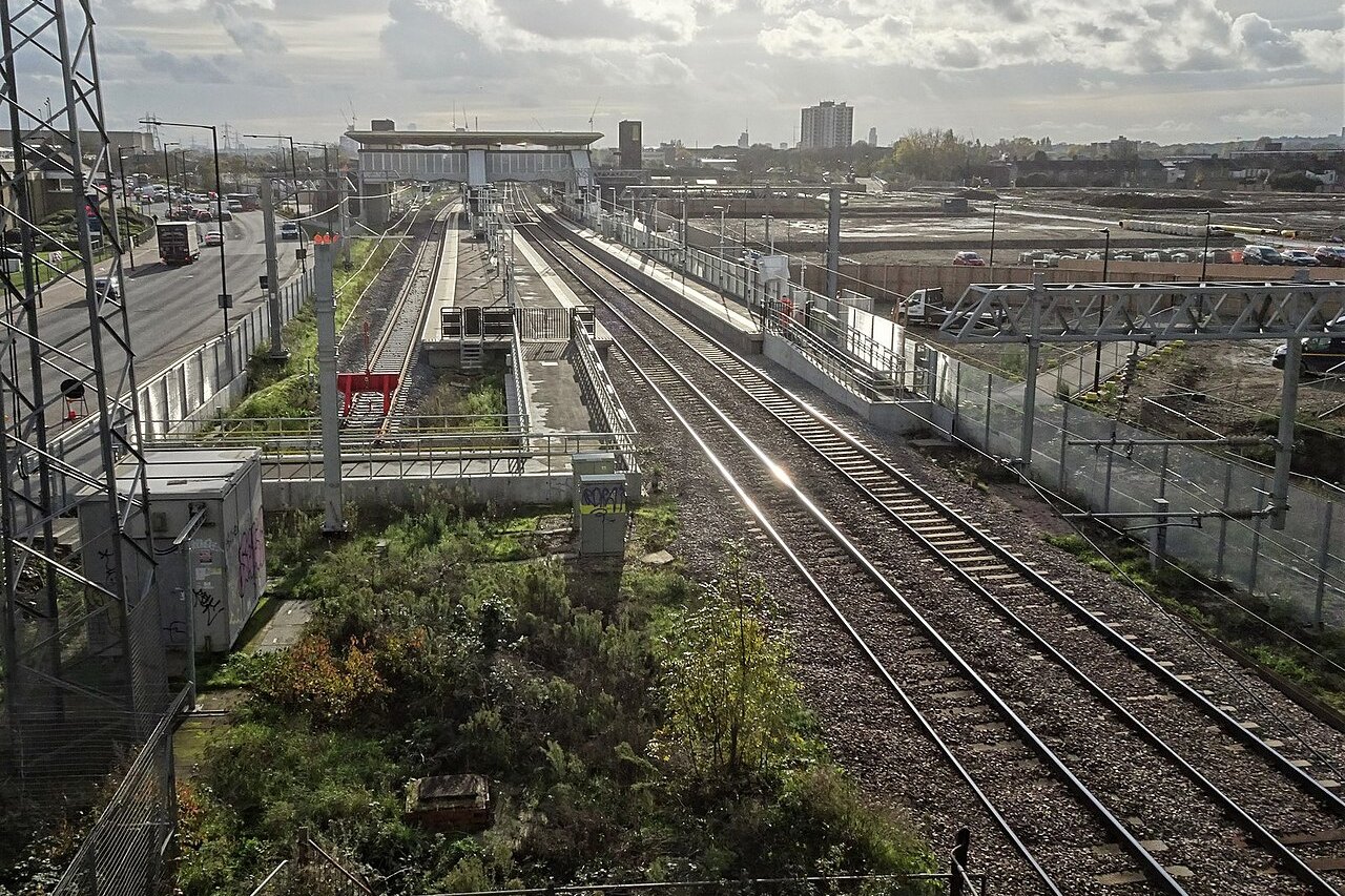 Meridian Water railway station seen from a footbridge, with its platforms, tracks and the station building under a cloudy sky beside the regeneration site