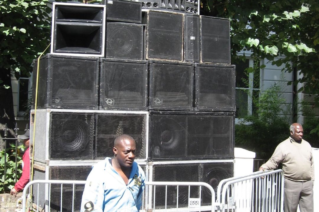 A static sound system stack of bass bins and horns set up on a west London street at Notting Hill Carnival, with crowd barriers in front