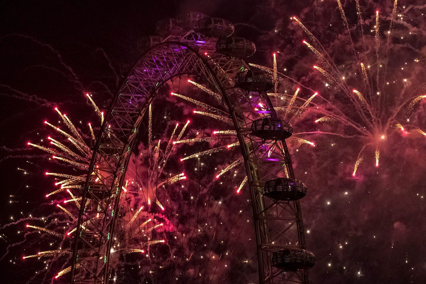 Fireworks bursting over the London Eye at midnight on New Year's Eve, reflected in the Thames