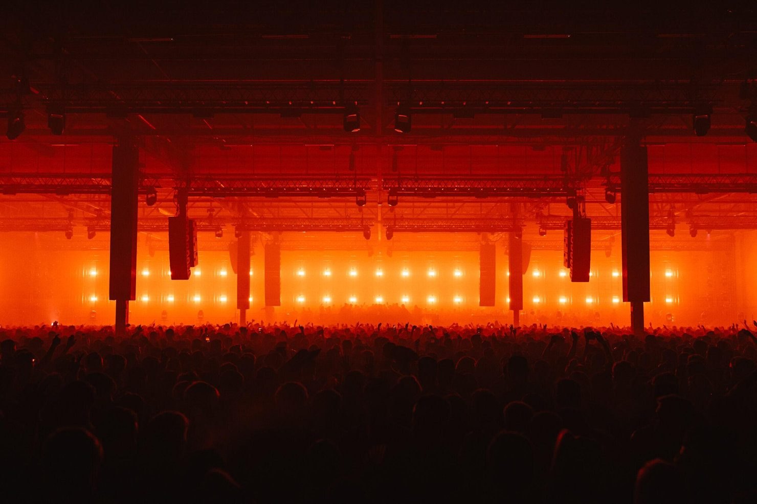 The X Room at Drumsheds bathed in orange light, thousands of people facing a wall of lights under the warehouse roof