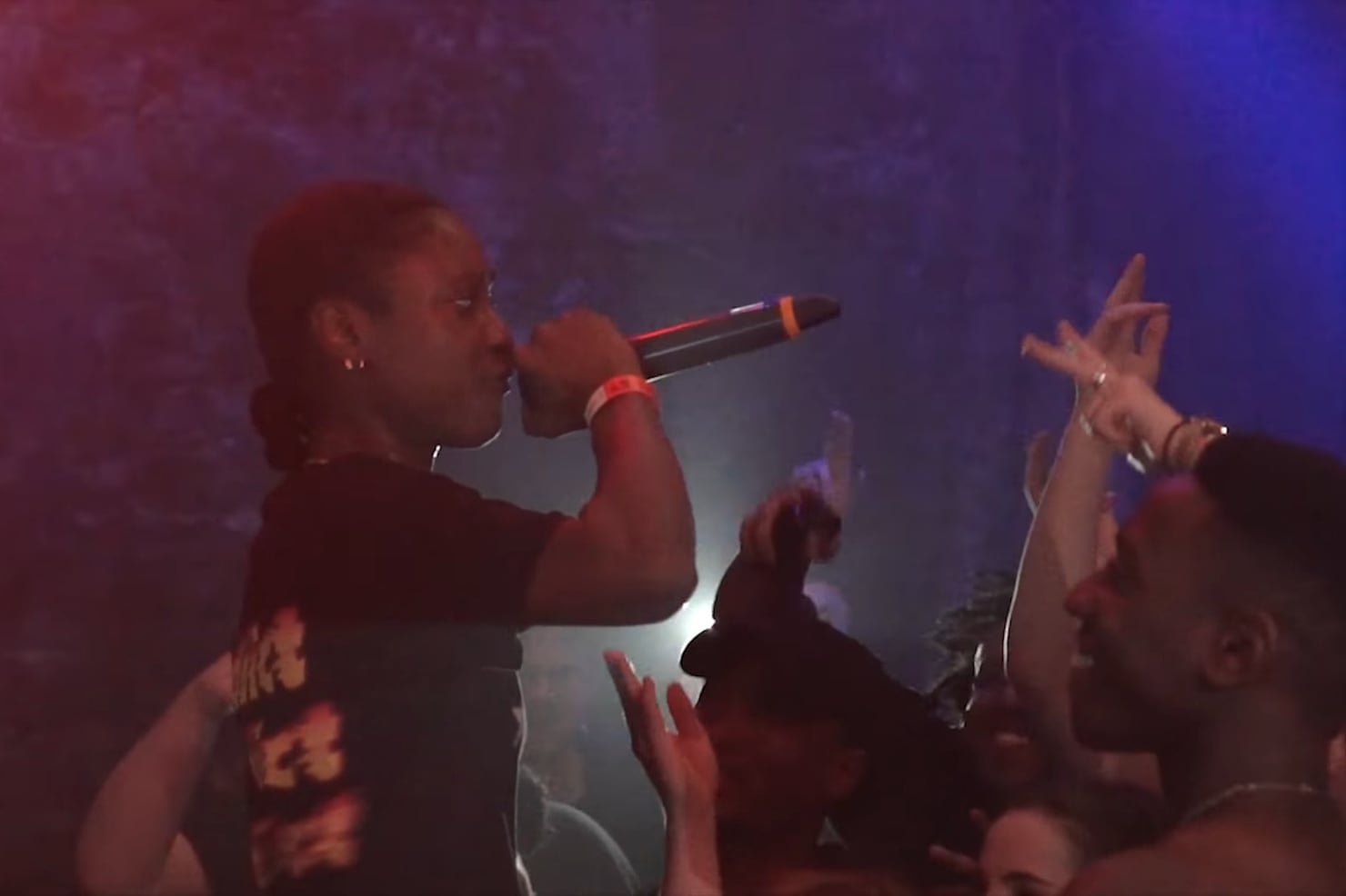 Flohio performing into a microphone on stage at The Warehouse Project in Manchester, lit from behind