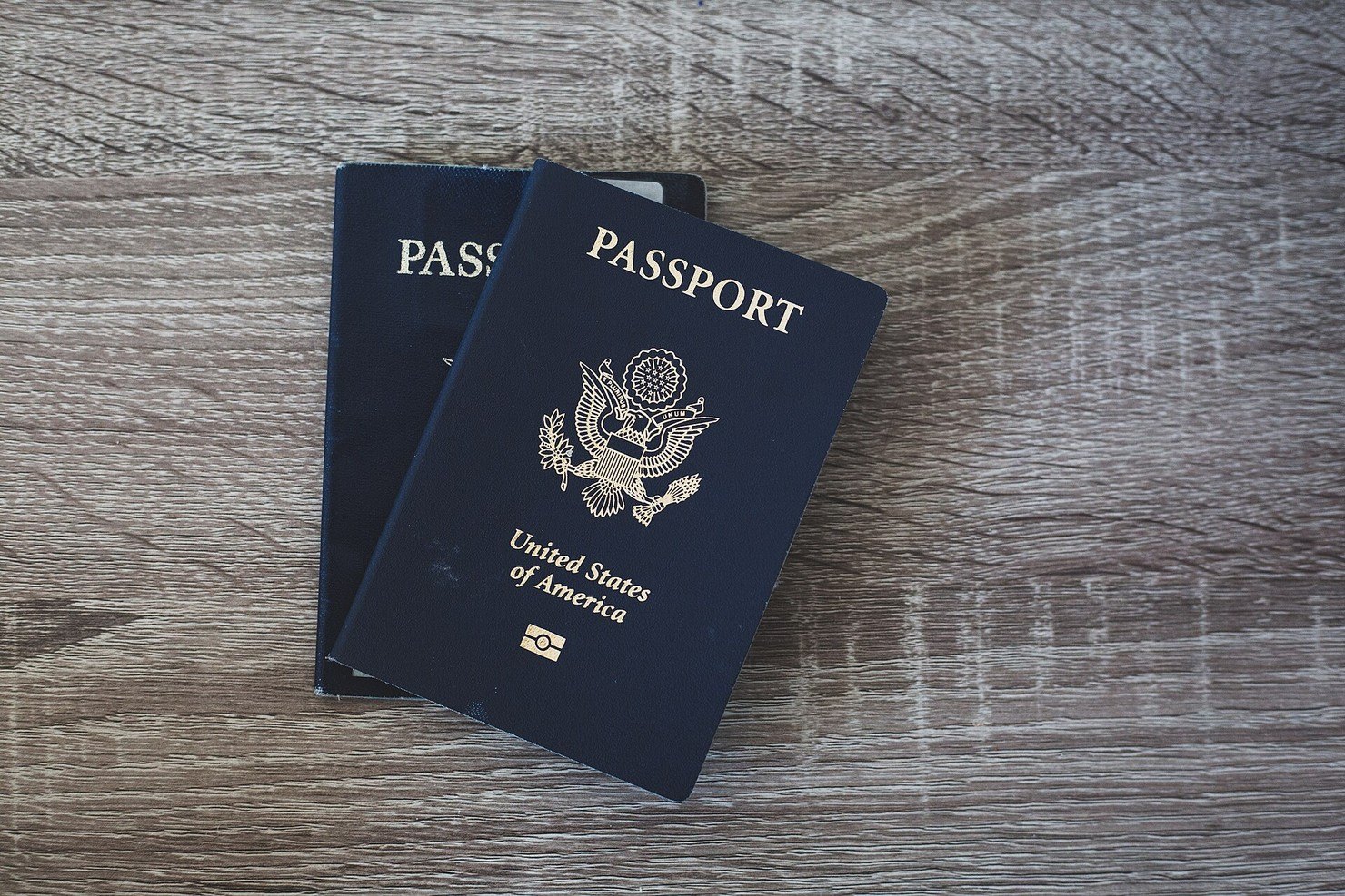 Two dark blue passports lying on a grey wooden tabletop, one overlapping the other