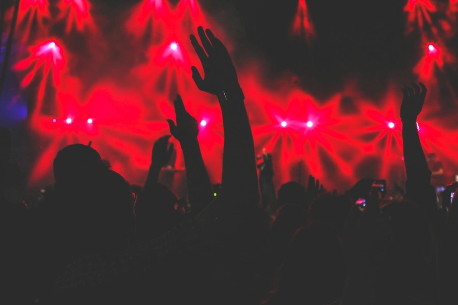 A rave crowd with hands up under red lasers