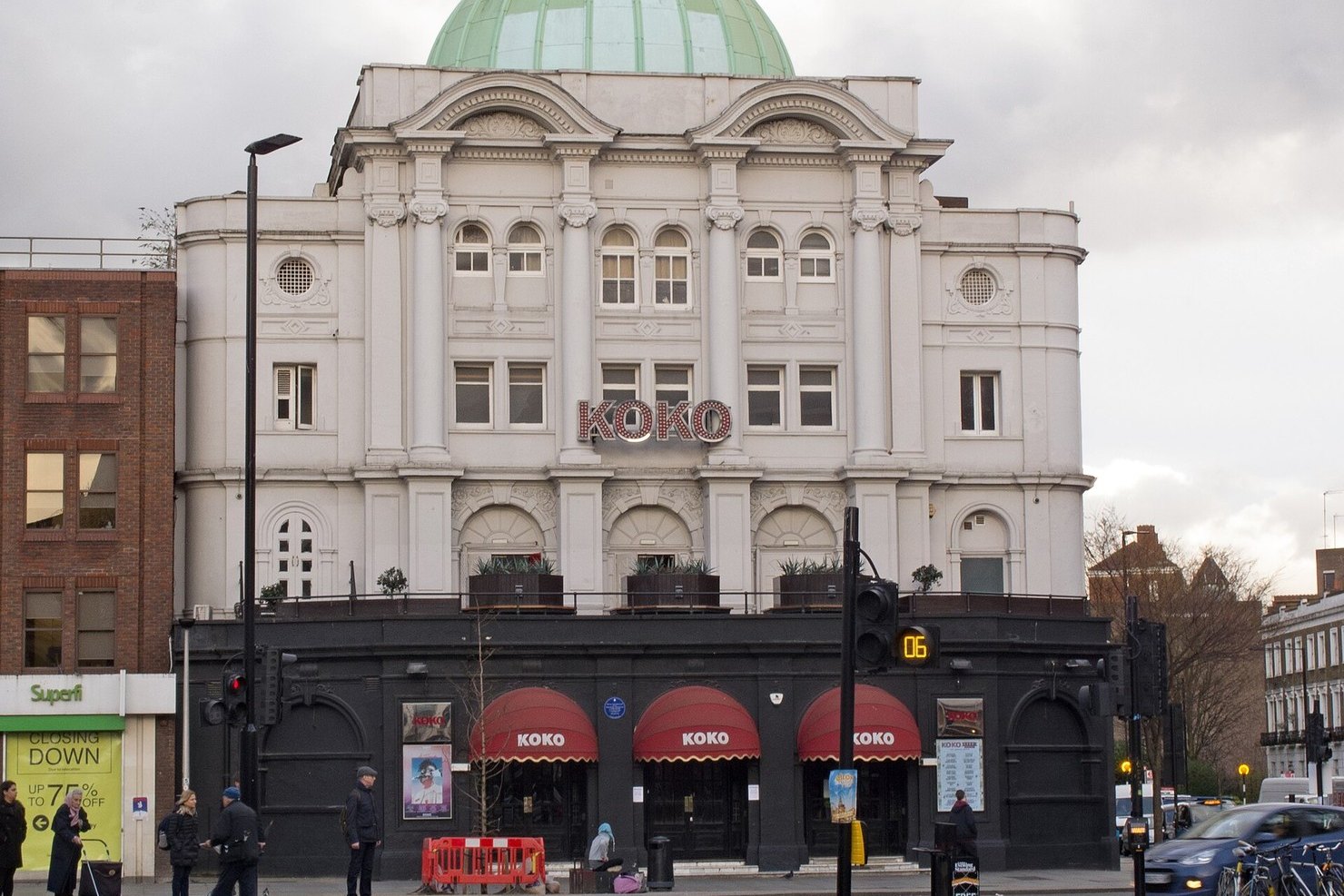 The white stucco facade of KOKO on Camden High Street under its green copper dome, red KOKO awnings over the doors and people crossing at the junction on a grey day